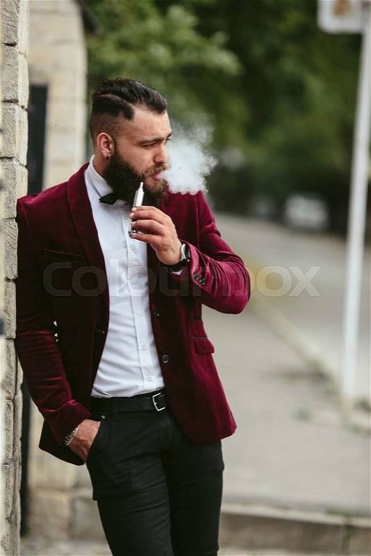 Rich man with a beard smokes electronic cigarette, stock photo
