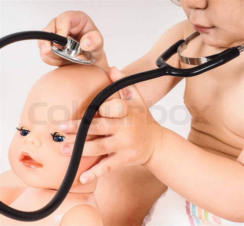 Toddler running a health check on a hairless doll with a stethoscope, stock photo