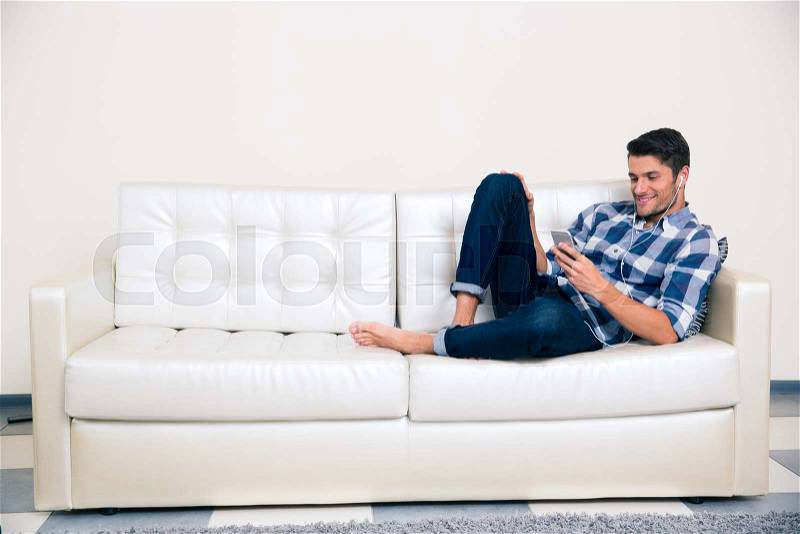 Portrait of a casual man with headphones using smartphone on the sofa , stock photo