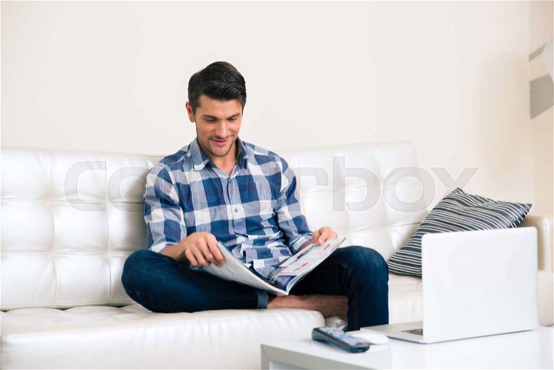 Portrait of a man reading magazine on the sofa at home , stock photo