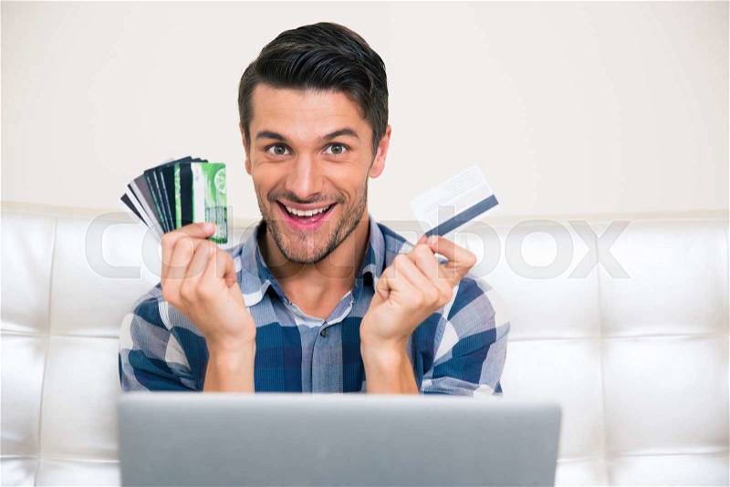 Portrait of a cheerful man holding credit cards at home, stock photo