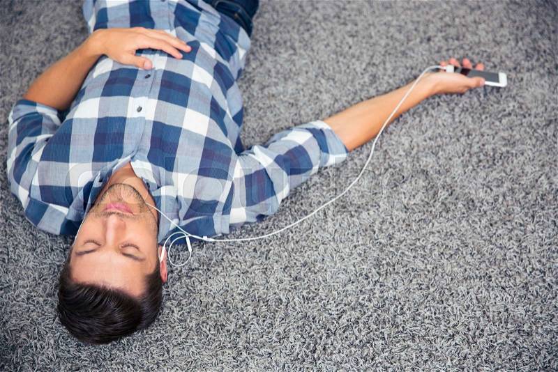 Portrait of a young man listening music in headphones on the floor at home, stock photo