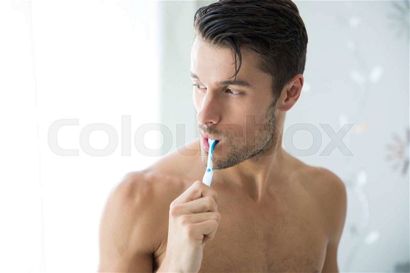 Portrait of a handsome man brushing teeth and looking away, stock photo