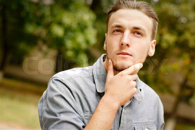 Portrait of a pensive young man with a beard, against a background of trees, stock photo