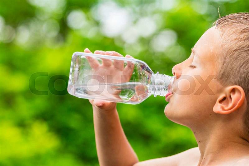 Closeup of young boy drinking pure tap water from transparent plastic drinking bottle while outdoors on a hot summer day, stock photo