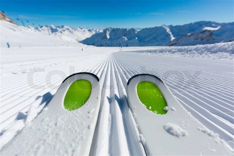 Pair of new skis standing on the fresh snow on newly groomed ski slope at ski resort on a sunny winter day, stock photo