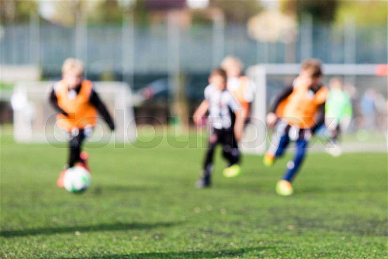 Out of focus shot of young children playing soccer on green soccer pitch, stock photo