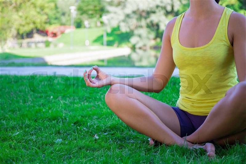 Yoga concept - close up of young woman sitting in lotus pose in summer park, stock photo