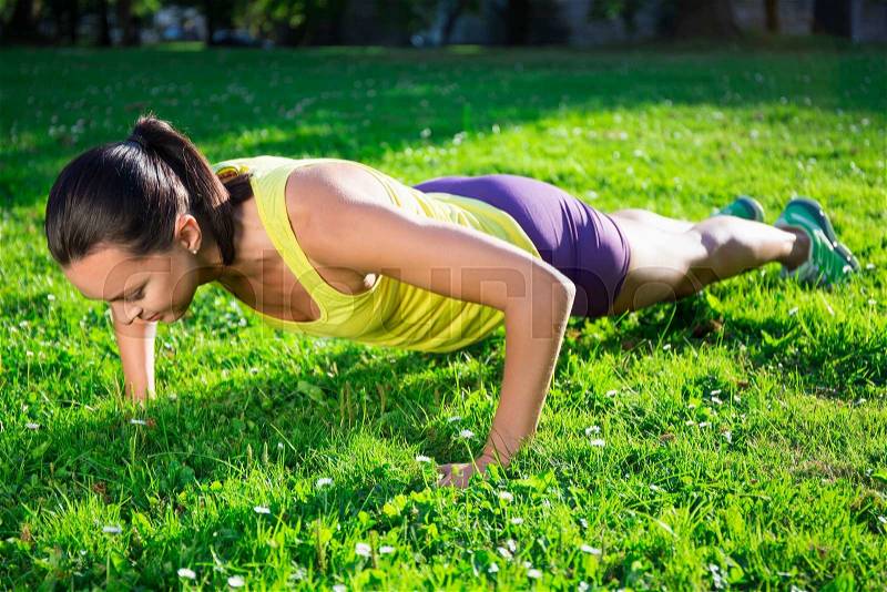 Beautiful woman doing push up exercise in summer park, stock photo