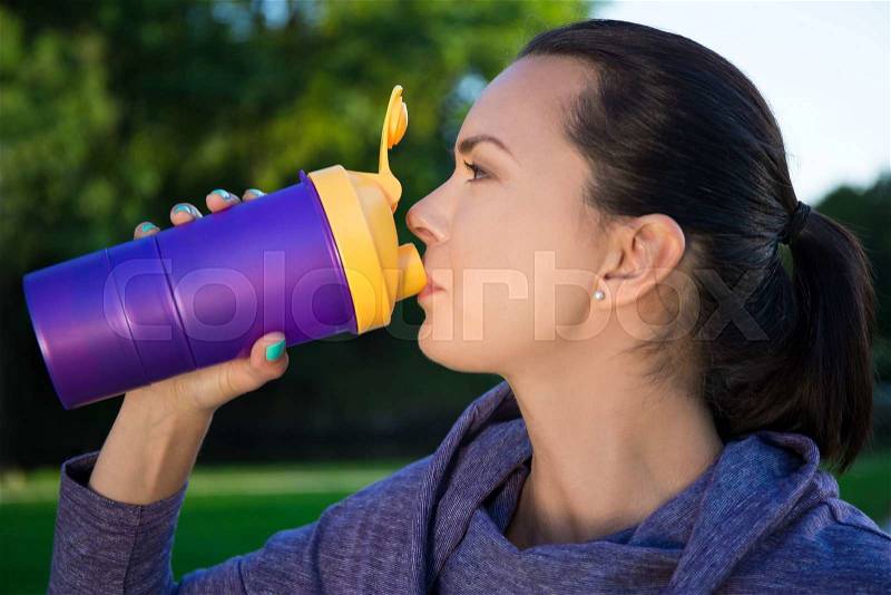 Close up of young beautiful woman drinking water from bottle in park, stock photo