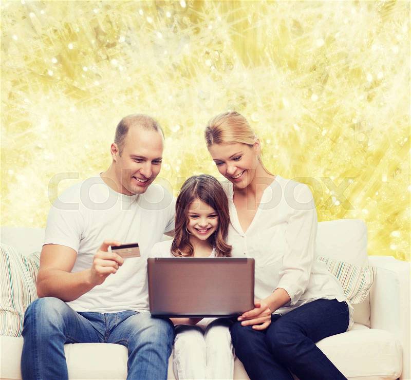 Family, holidays, shopping, technology and people concept - happy family with laptop computer and credit card over yellow lights background, stock photo