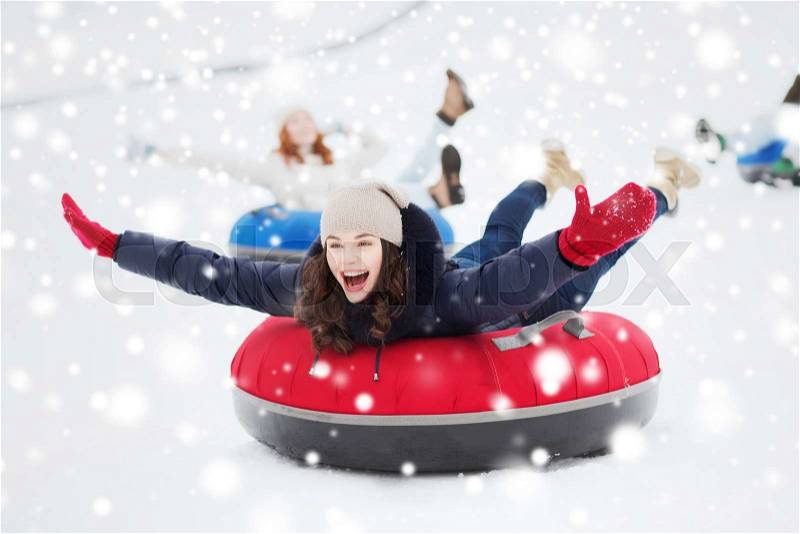 Winter, leisure, sport, friendship and people concept - group of happy friends sliding down on snow tubes, stock photo