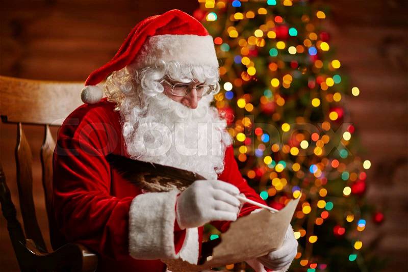 Santa Claus answering Christmas letter by sparkling firtree, stock photo
