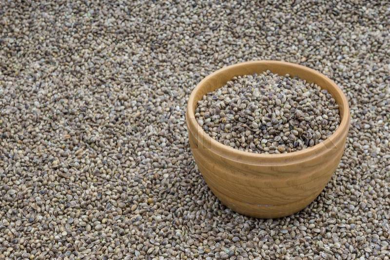 Side view of wooden bowl with hemp seeds standing on a hemp seed background, stock photo