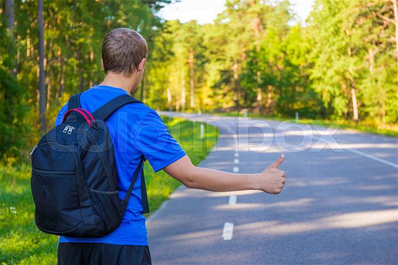 Back view of young man hitchhiking on forest road, stock photo