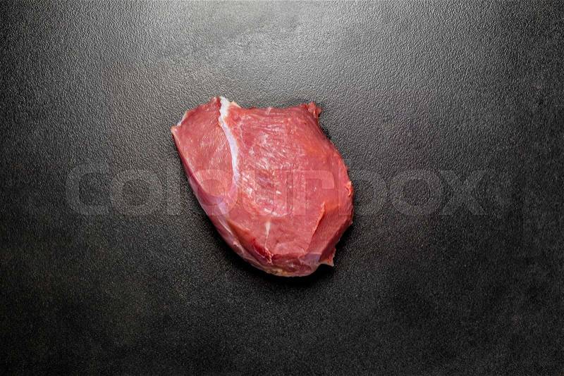 Overhead view eyes round beef meat on black background. Piece of fresh raw beef. Big piece of red meat on a dark textured ceramic background, stock photo