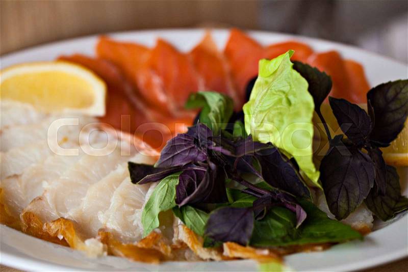 Fish appetizer with lemon and lettuce on white plate in restaurant.Healthy food.Tasty diet, stock photo