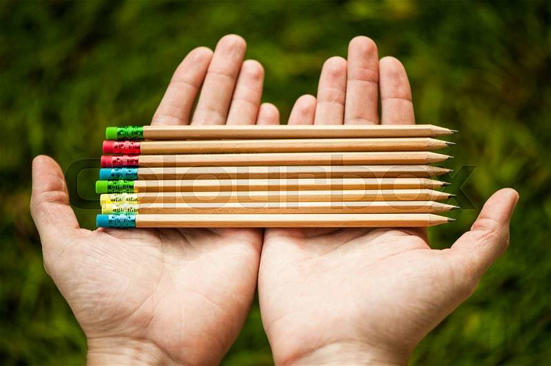 Row of color pencils in hands on green bush background.Art.Creativity, stock photo