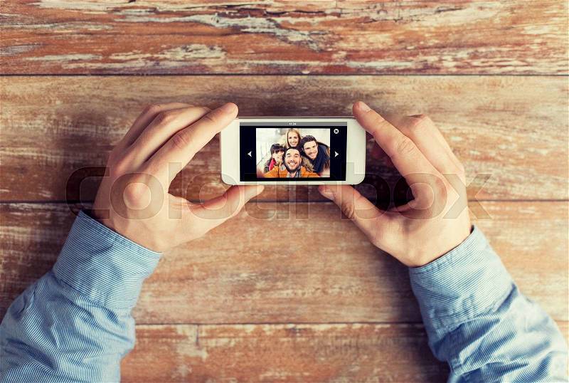 People, memory, relations and technology concept - close up of male hands holding smartphone with photo of happy friends on screen at table, stock photo