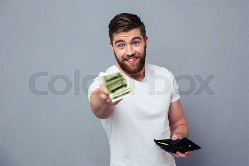 Portrait of a happy casual man giving money at camera over gray background, stock photo