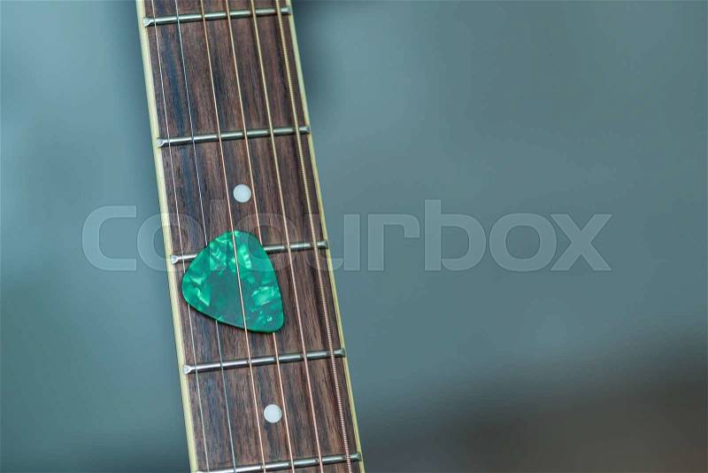 Colorful green guitar pick on finger board, as abstract background, stock photo