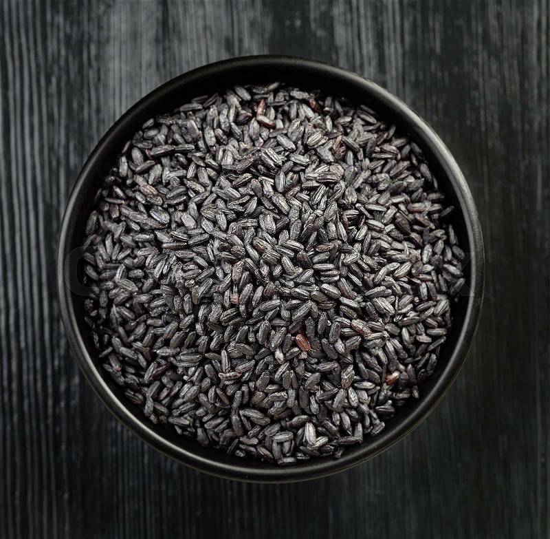 Bowl of black wild rice on black wooden table, top view, stock photo