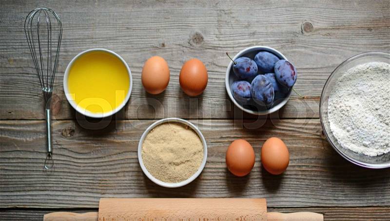 Baking cake in rural kitchen - dough recipe ingredients (eggs, flour, butter, sugar) and rolling pin and plums on vintage wood table from above. , stock photo