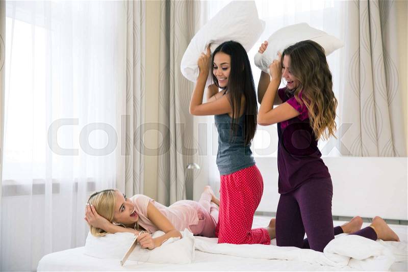 Portrait of a girlfriends fighting with pillows at home, stock photo
