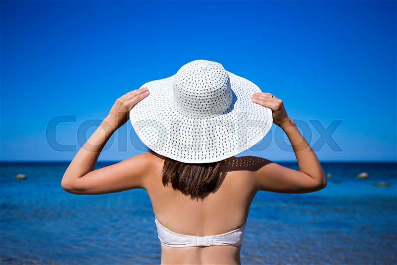 Travel concept - back view of slim woman in bikini and hat looking at the sea, stock photo