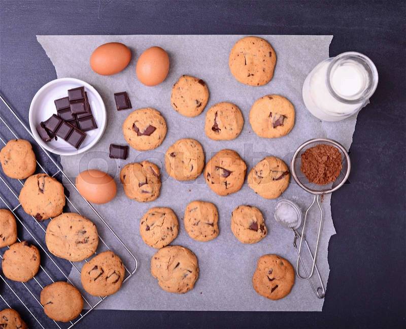 Home baked chocolate cookies on cooling rack and baking paper with ingredients on black background, stock photo