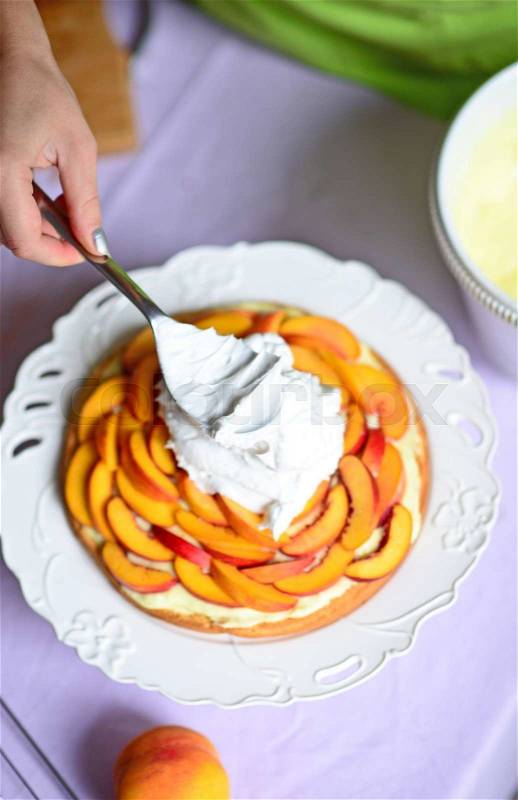 Woman hand put whipped cream on peach cake, stock photo