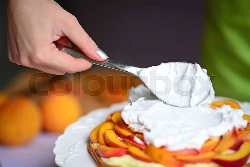 Woman hand put whipped cream on peach cake, stock photo