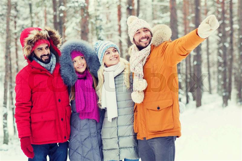 Love, relationship, season, friendship and people concept - group of smiling men and women pointing finger in winter forest, stock photo