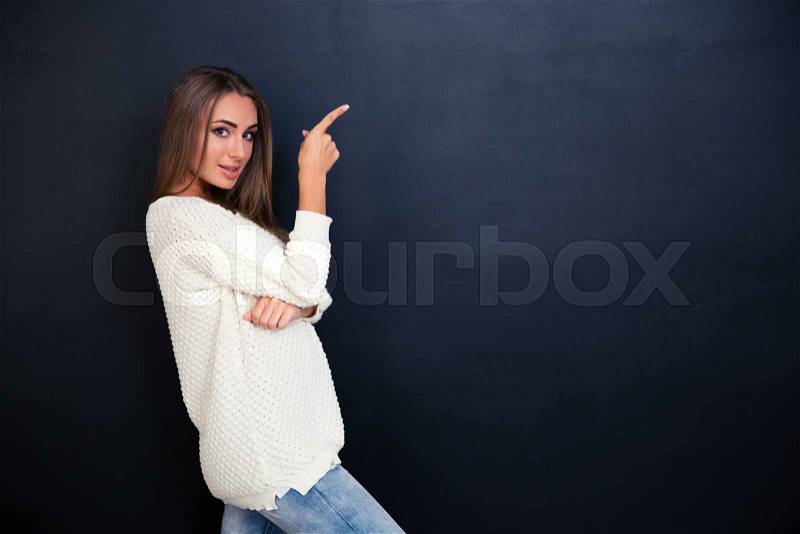 Portrait of a happy girl pointing finger away over gray background and looking at camera, stock photo