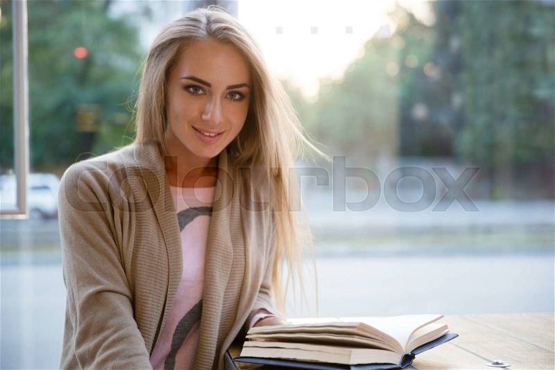 Portrait of a happy cute girl sitting with book in cafe and looking at camera, stock photo