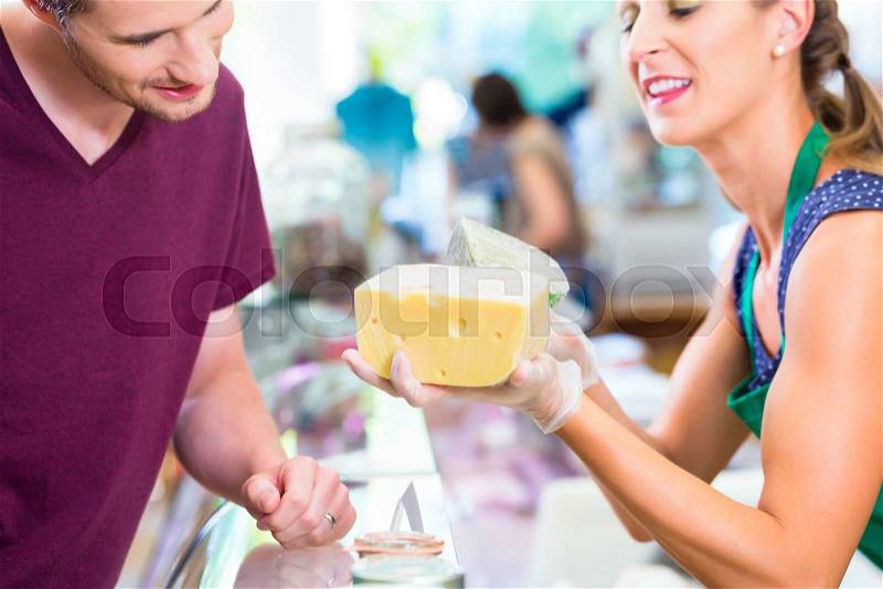 Saleswoman at organic supermarket counter offering costumer cheese, stock photo