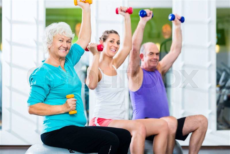 Senior man and women with fitness trainer in gym lifting barbells as sport exercise, stock photo