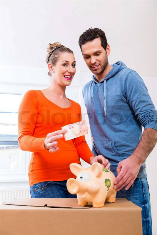 Couple saving money by moving house, piggybank standing on packing case, stock photo