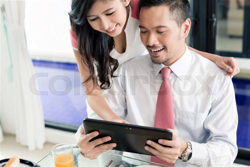 Asian couple having breakfast before man goes to office, he is checking the emails or news with his wife, stock photo
