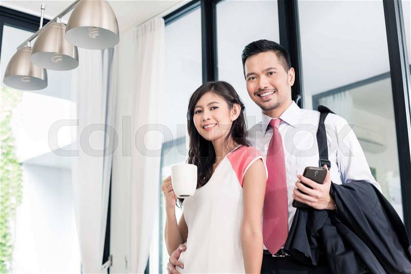 Asian couple having breakfast before man goes to office, standing in their home, stock photo