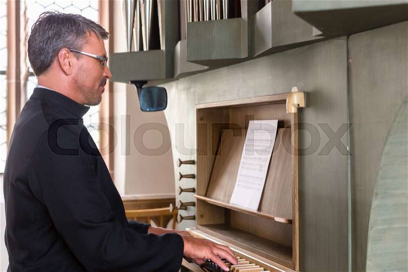 Pastor making music playing organ in church, stock photo