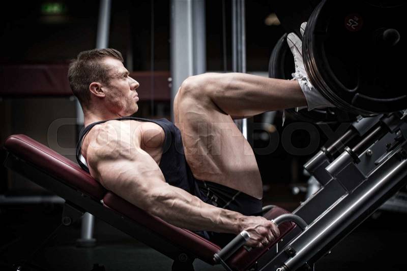 Man in gym training at leg press to define his upper leg muscles, stock photo