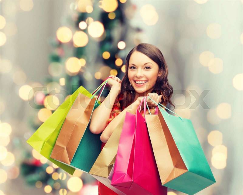 Sale, gifts, holidays and people concept - smiling woman with colorful shopping bags over living room and christmas tree background, stock photo