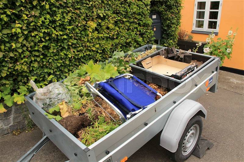 A trailer full with garden waste, cardboard and an old blue folding bed in the residential area in the city Roskilde in Denmark in the summer, stock photo