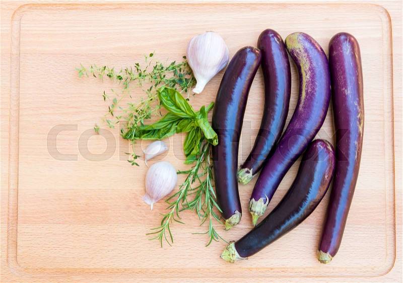 Purple japanese eggplants with herbs and garlic on wooden cutting board, stock photo