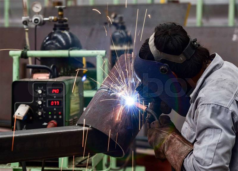 Welder in factory with protective equipment welding pipe, stock photo