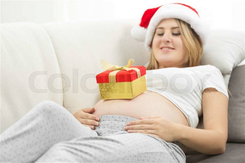 Cute pregnant woman getting ready for Christmas posing with gift box, stock photo