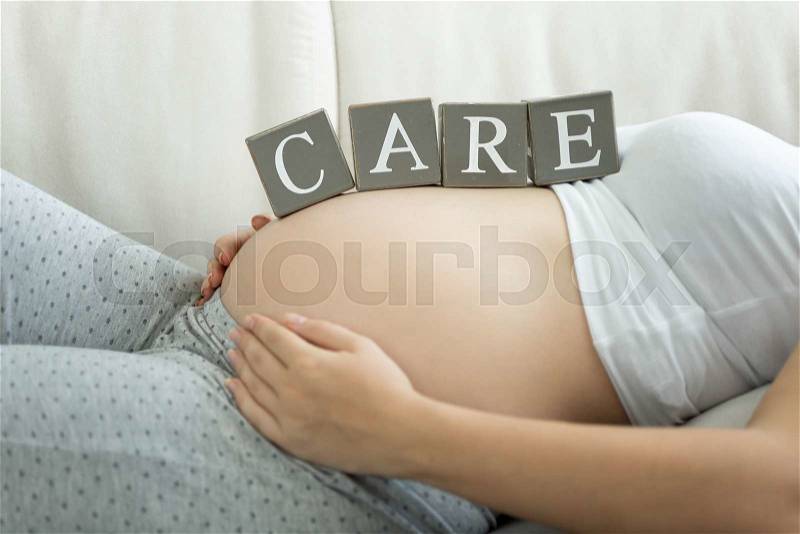 Letters on wooden blocks making word Care on pregnant women tummy, stock photo