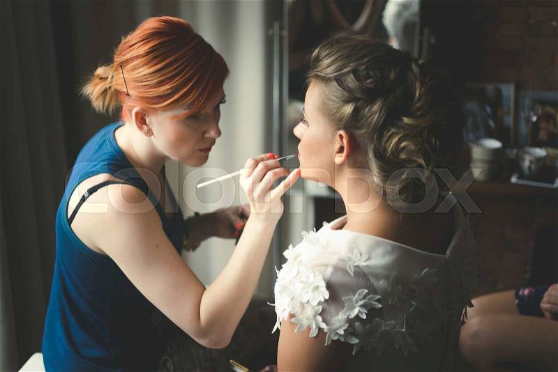 Toned portrait of makeup artist preparing blonde bride at morning, stock photo