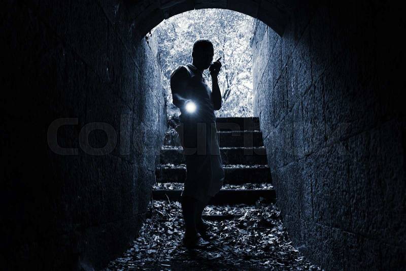 Young man with radio set and flashlight enters the stone tunnel and looks in the dark, monochrome photo, stock photo